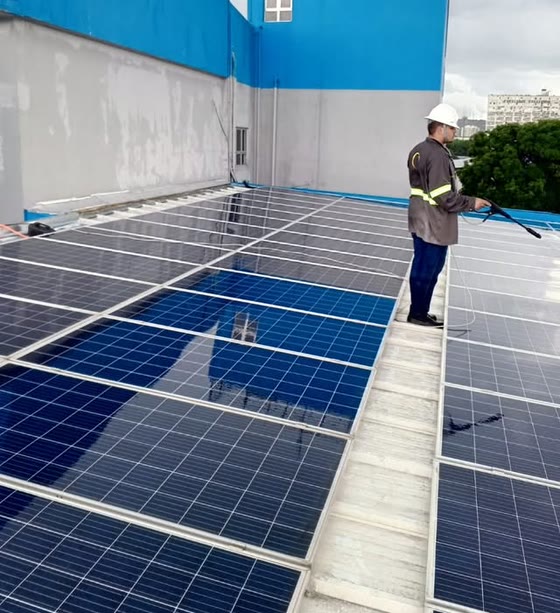 Técnico uniformizado com capacete lavando painéis solares em um telhado